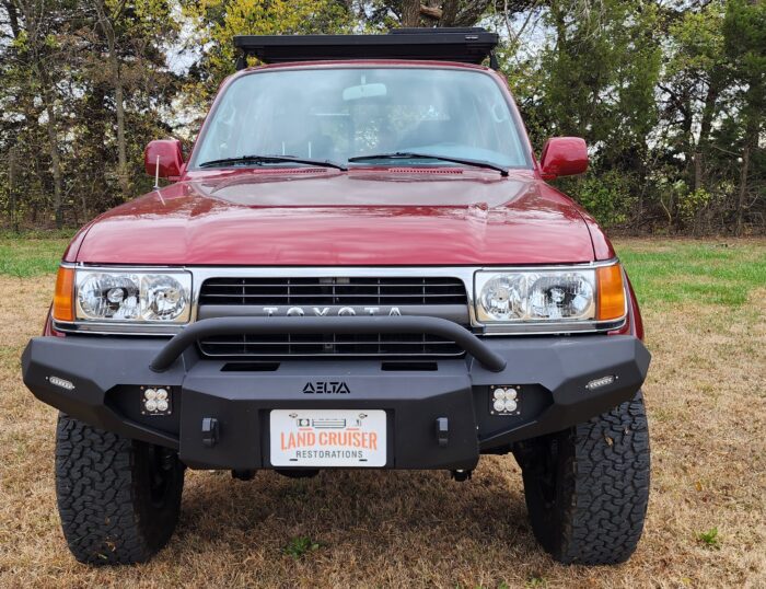 Front view of maroon 1991 Toyota FJ80 Land Cruiser restomod with Delta off-road bumper, LED pod lights, and chrome grille, restored by Land Cruiser Restorations