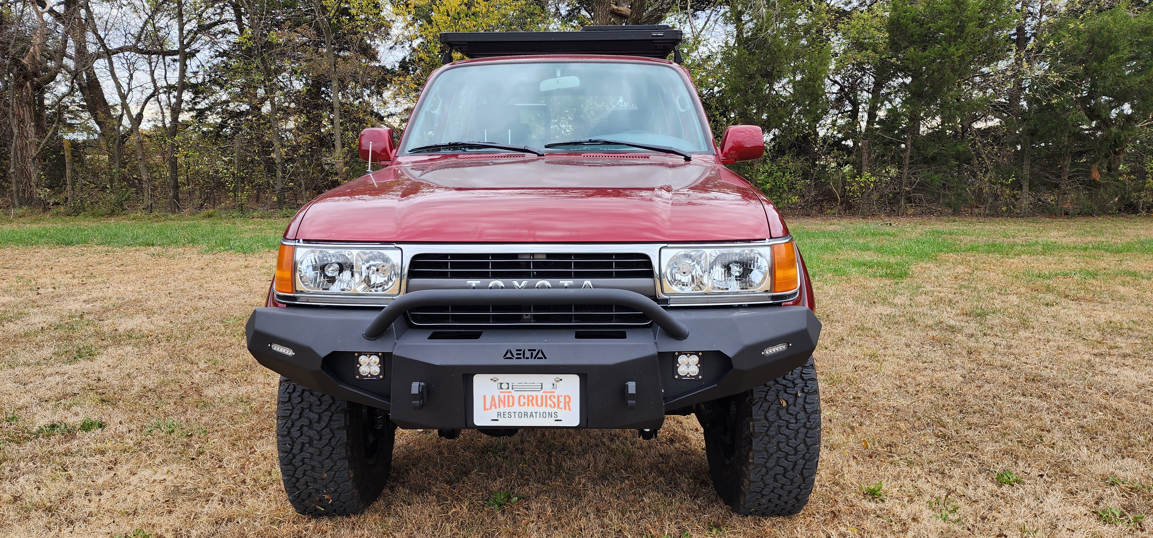 Front view of maroon 1991 Toyota FJ80 Land Cruiser restomod with Delta off-road bumper, LED pod lights, and chrome grille, restored by Land Cruiser Restorations