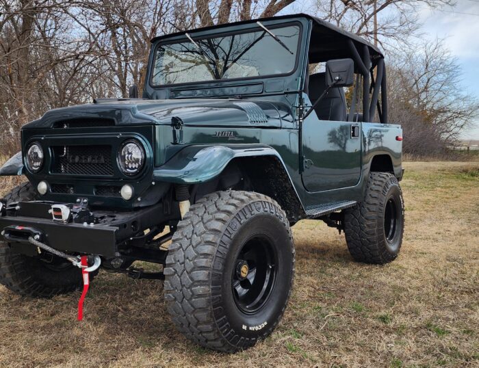 Dark green 1966 Toyota FJ40 Land Cruiser restoration with bikini top, black roll cage, custom front bumper with winch, and Mickey Thompson tires, restored by Land Cruiser Restorations